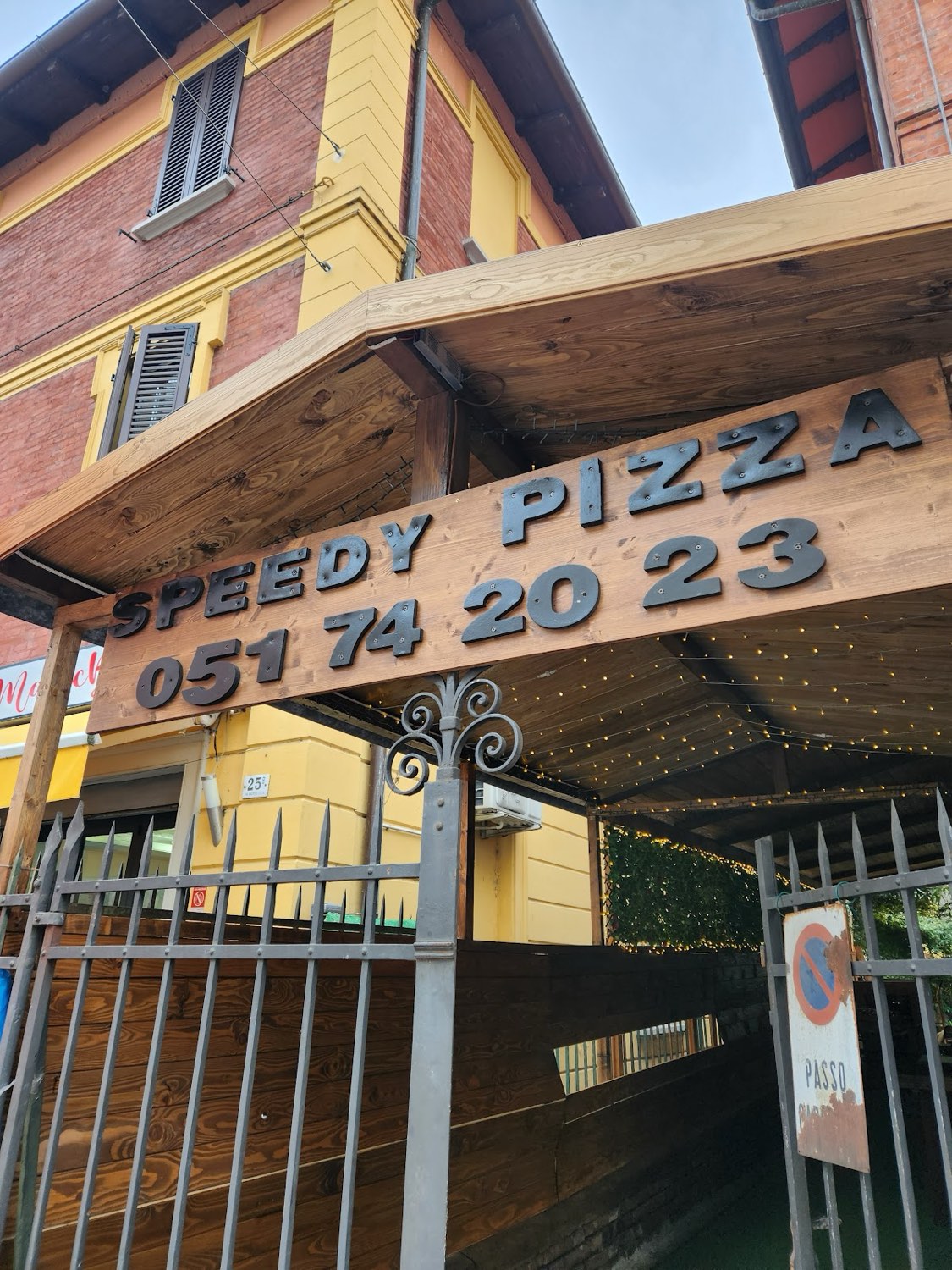 L'ingresso di Speedy Pizza: insegna in legno con lettere nere e il numero di telefono
