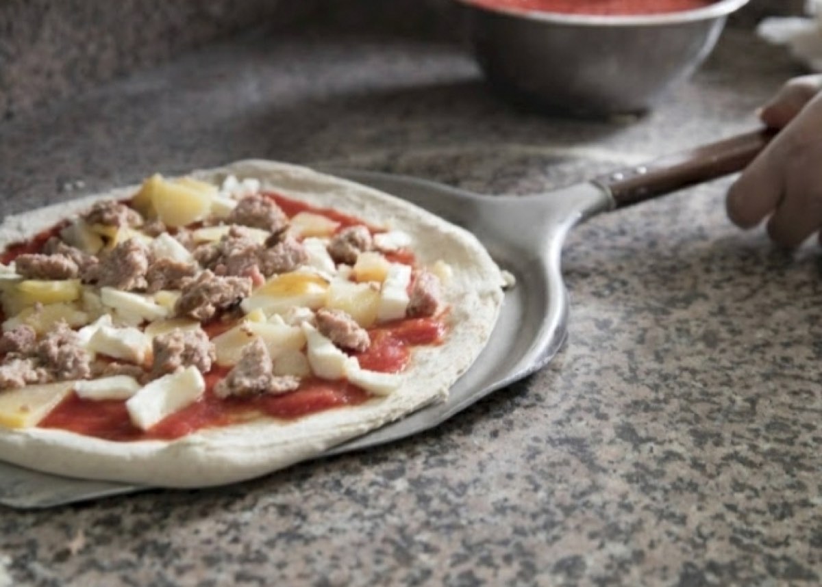 Pizza farcita con salsiccia e patate sulla pala, prima del forno